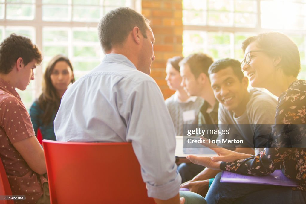 Woman with digital tablet speaking to man at group therapy session