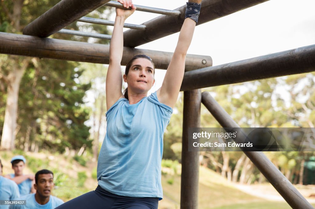 Determined woman crossing monkey bars on boot camp obstacle course