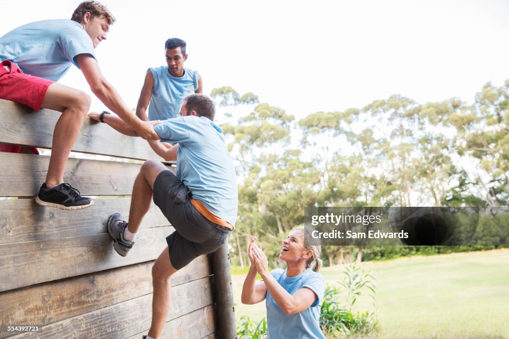 Teammates helping man over wall on boot camp obstacle course