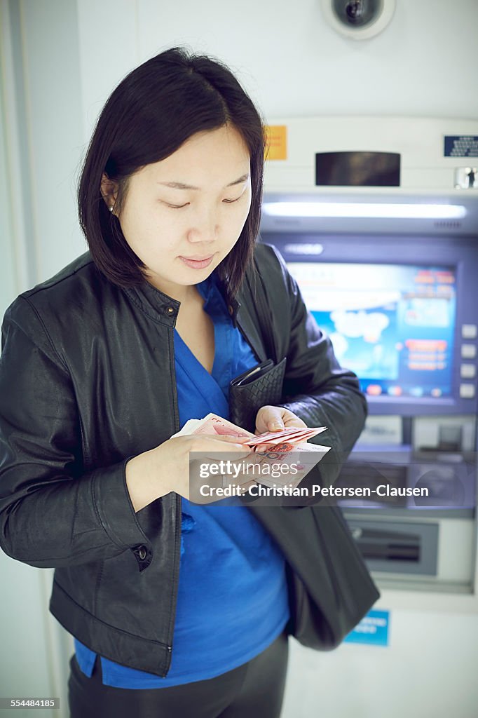 Young woman counting cash at cashmachine