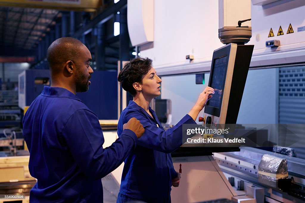 Female & male steel workers, operating big machine