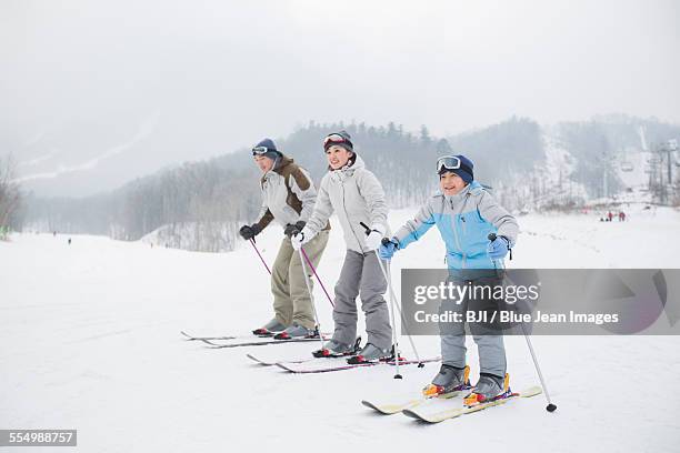young family skiing in ski resort - chinese father and son snow stock pictures, royalty-free photos & images