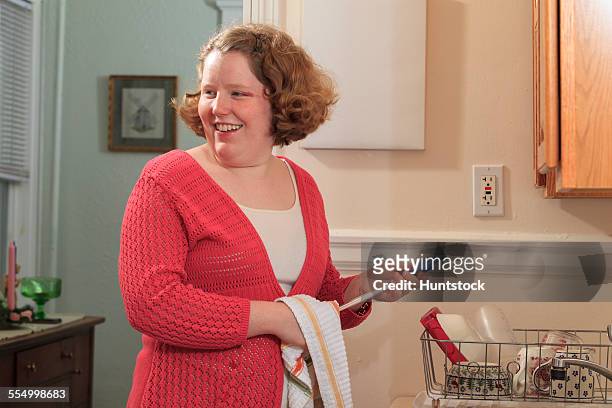 young woman with autism drying disher in her kitchen - hemangioma - fotografias e filmes do acervo
