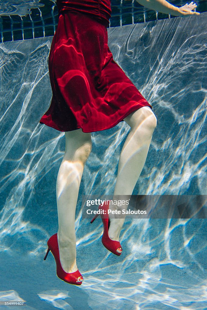 Mature woman wearing red dress and high heels, underwater view, low section