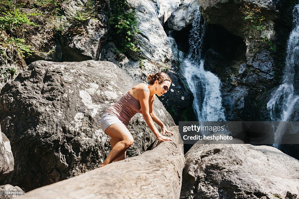 A woman climbing on rock near a waterfall