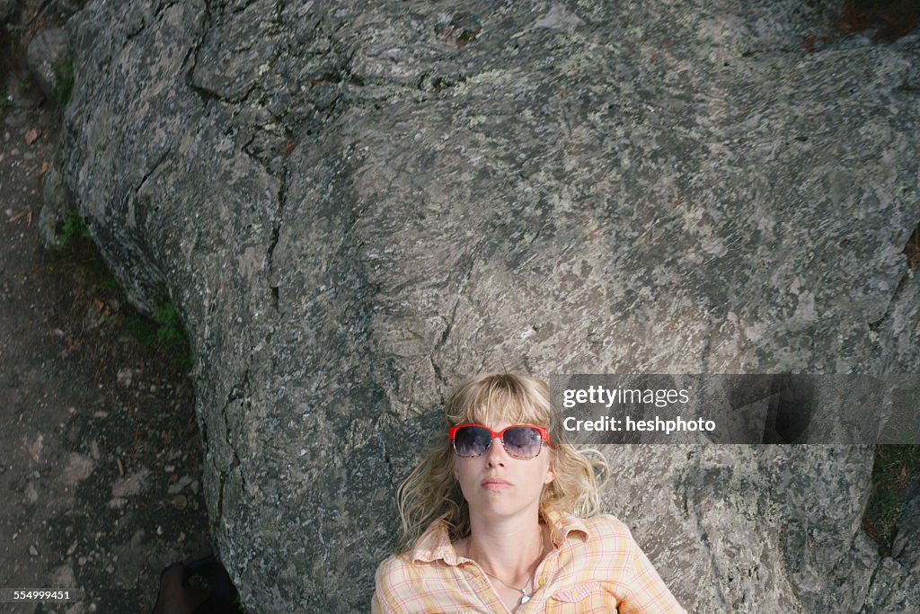 Young woman in sunglasses, lying on rock