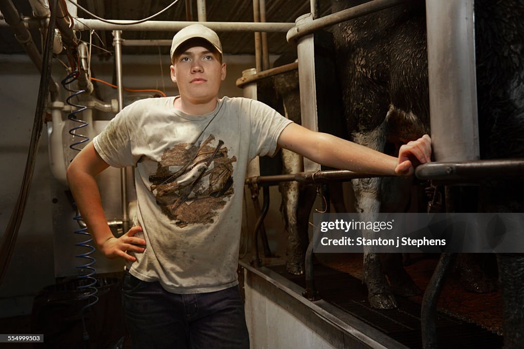 Portrait of teenage boy leaning on railing in dairy farm milking shed