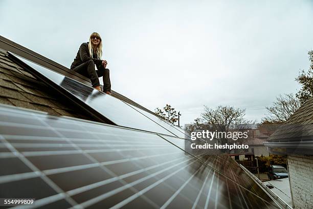 portrait of mid adult woman sitting on newly solar paneled house roof - eco house stockfoto's en -beelden