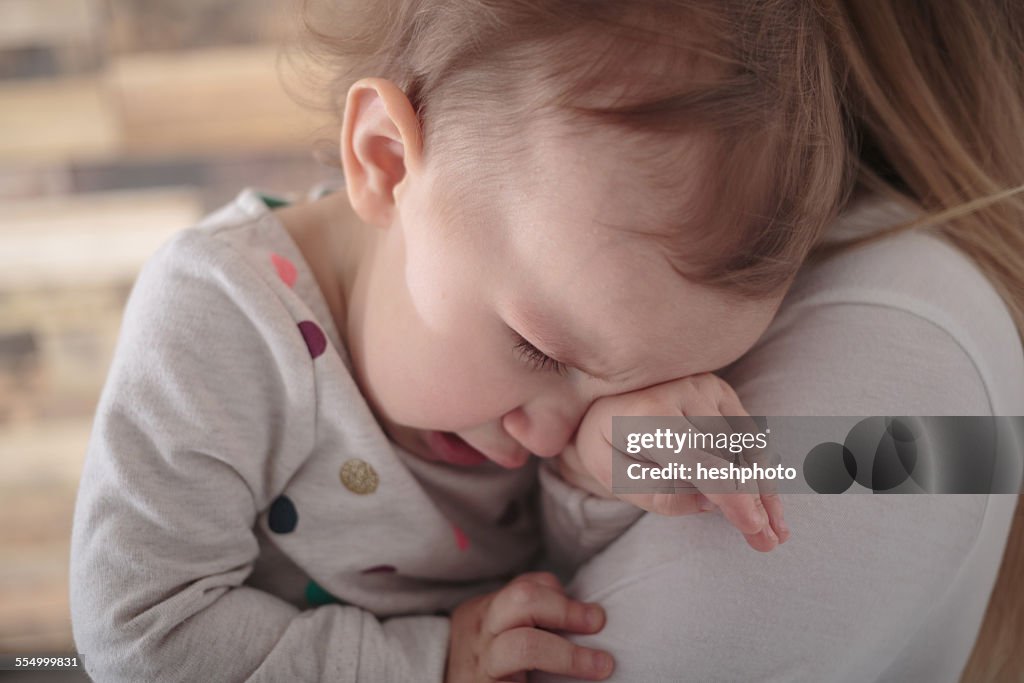 Toddler girl crying on mothers shoulder