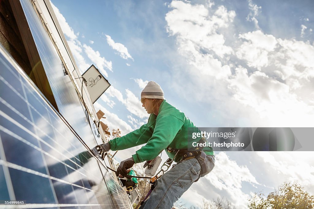 Construction crew member installing a solar panel on a house