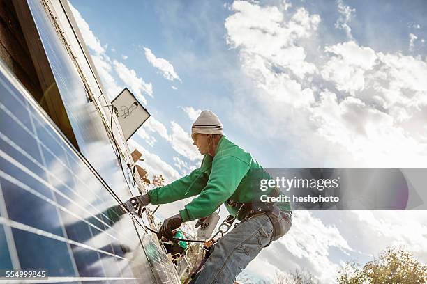 construction crew member installing a solar panel on a house - heshphoto - fotografias e filmes do acervo