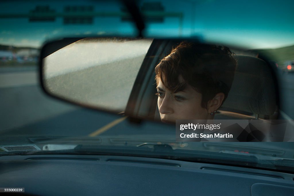Reflection of mid adult woman in car mirror