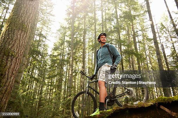 young man standing with mountain bike in forest, low angle view - low motivation stock pictures, royalty-free photos & images