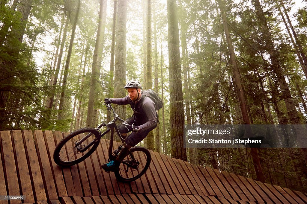 Mature man doing stunts on mountain bike, in forest