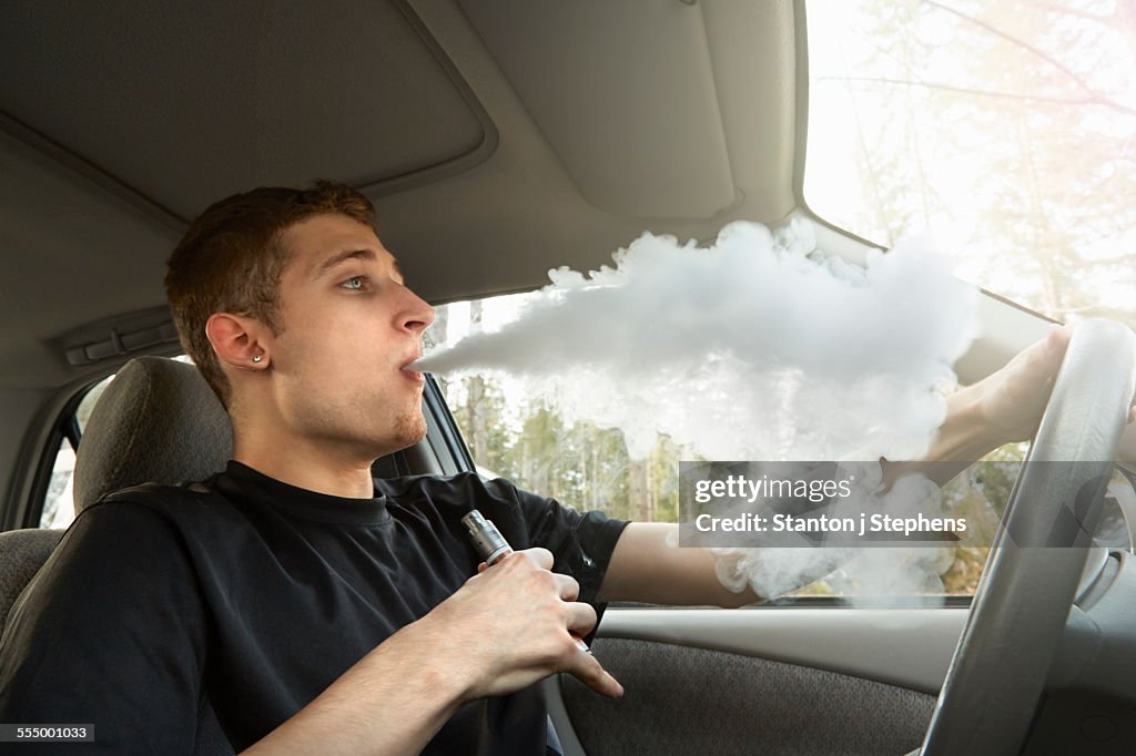 Young man driving car, smoking ecigarette