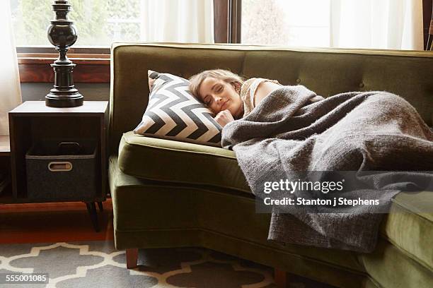 young woman lying on living room sofa wrapped in blanket - cobertor imagens e fotografias de stock