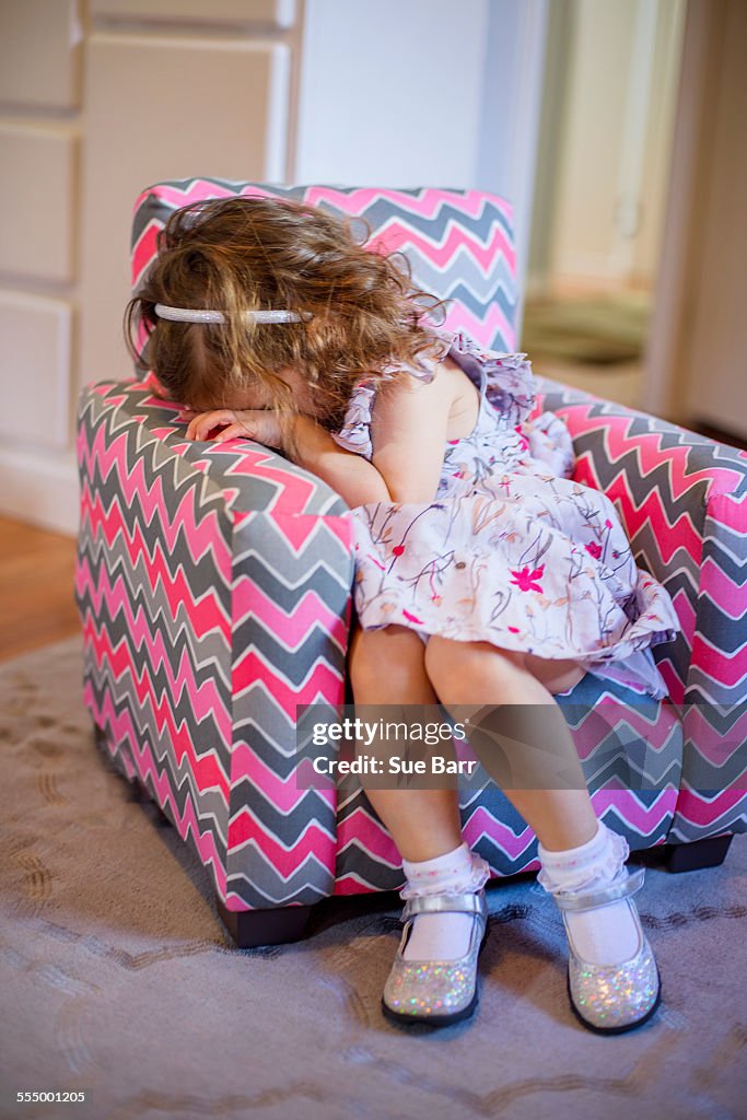 Female toddler with hiding her face on childs armchair