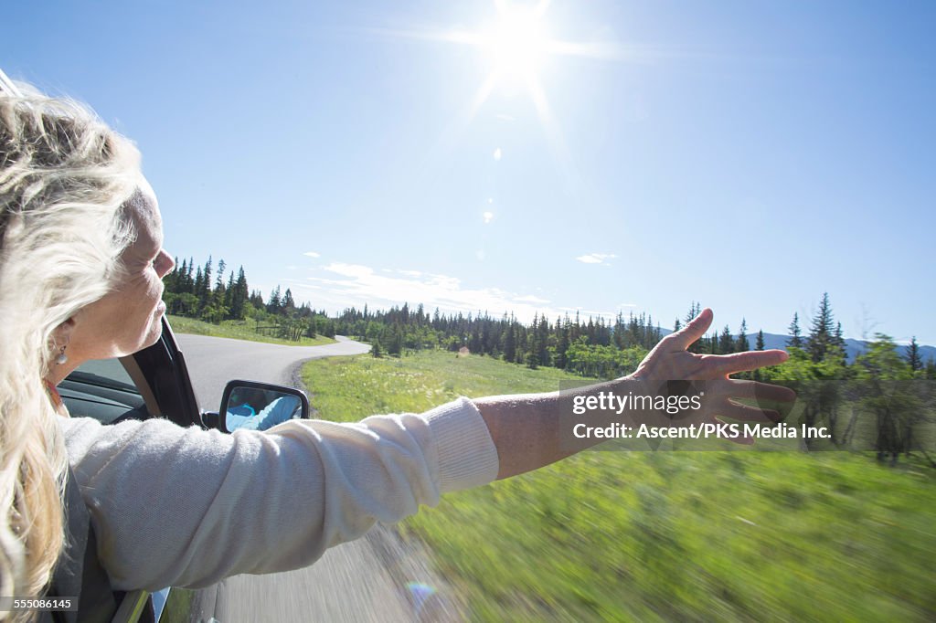 Woman stretches arm out of car window, rural road