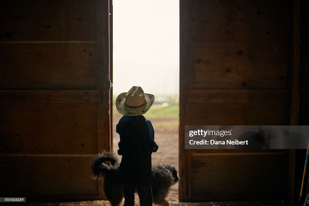 Boy and dog looking out barn doors