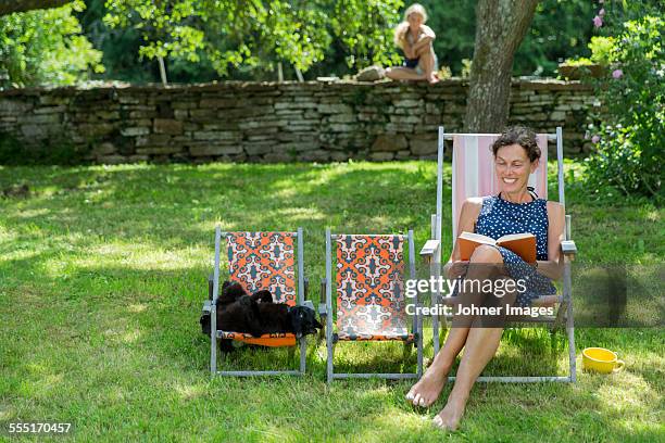 smiling mature woman reading book in garden - stone wall garden stock pictures, royalty-free photos & images