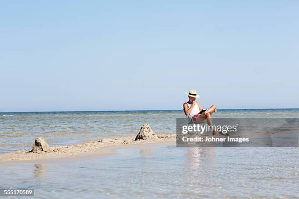 mature man reading book on beach - oland stock-fotos und bilder