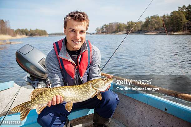 young man holding caught fish - young men fishing stock pictures, royalty-free photos & images
