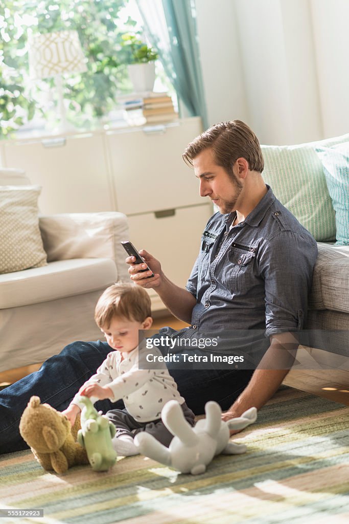 Father sitting on floor with little son (2-3 years) in living room and texting message