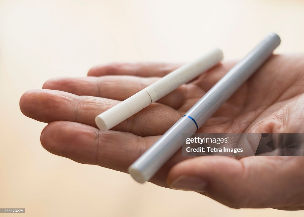 Close up of mans hand holding cigarette and e-cigarette