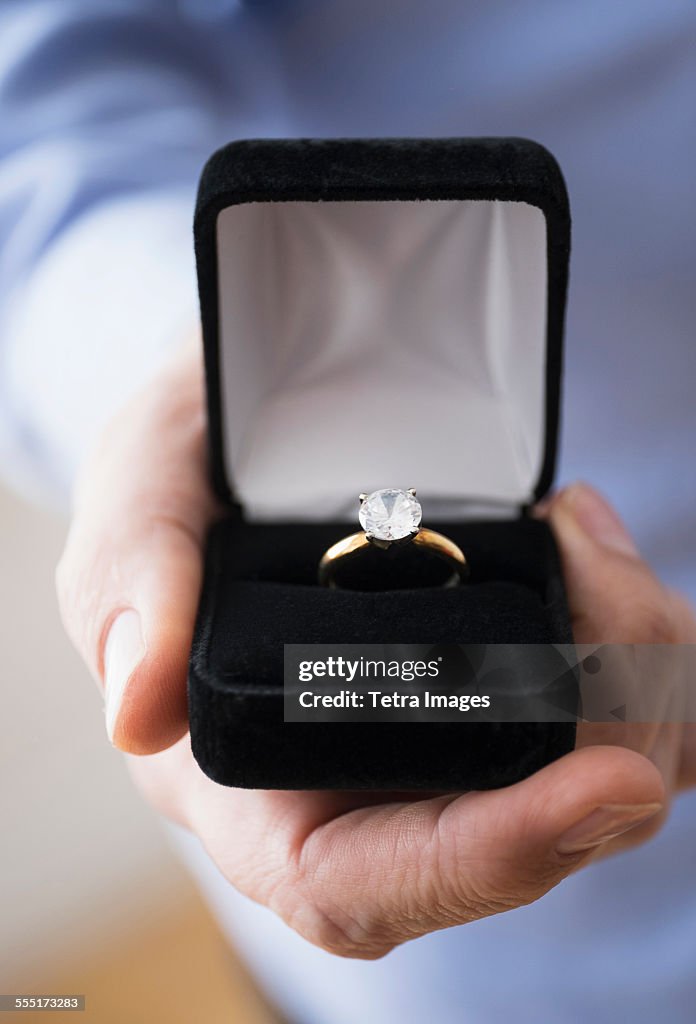 Close up of mans hand holding open box with engagement ring