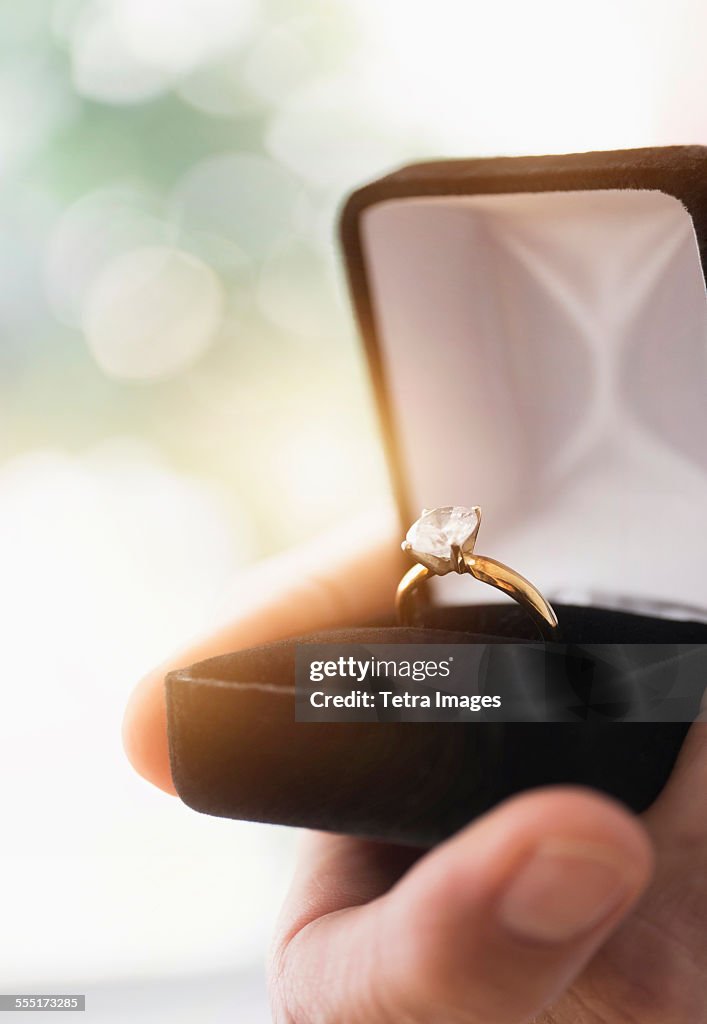 Close up of mans hand holding open box with engagement ring