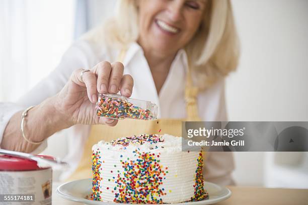 senior woman decorating cake - sugar sprinkles stock pictures, royalty-free photos & images