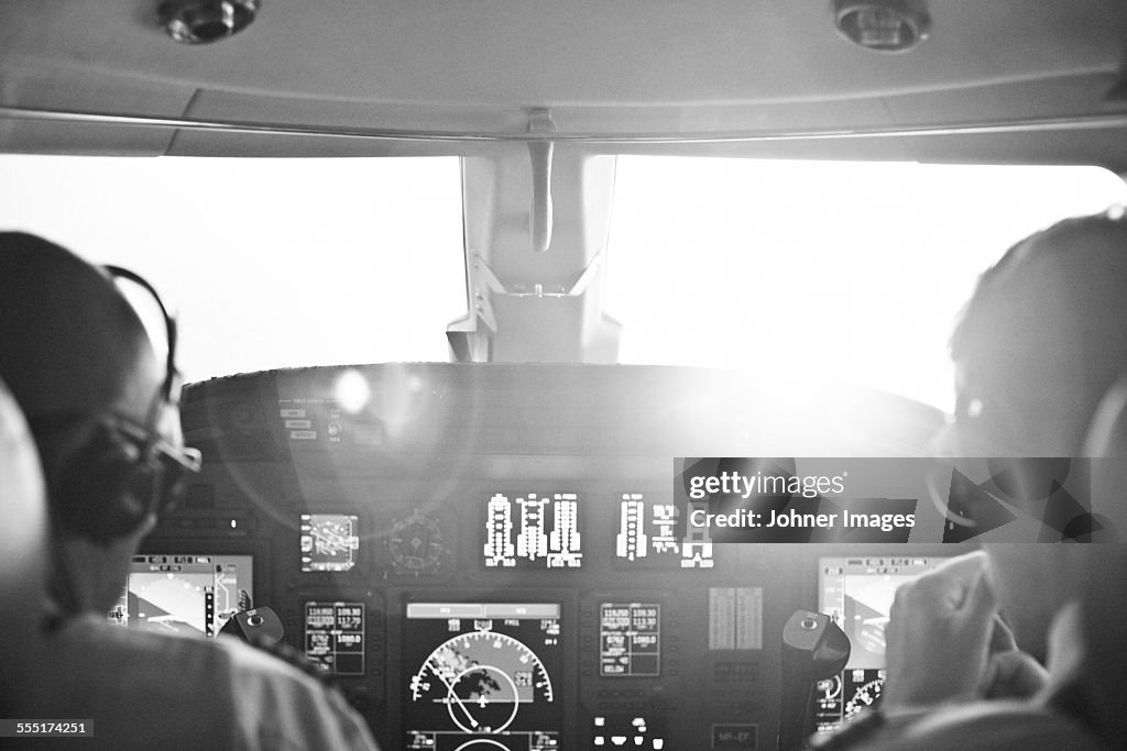 Rear view of two pilots sitting in cockpit of airplane