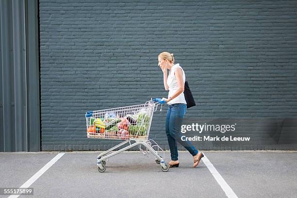 netherlands, tilburg, woman walking with shopping cart - cart stock-fotos und bilder