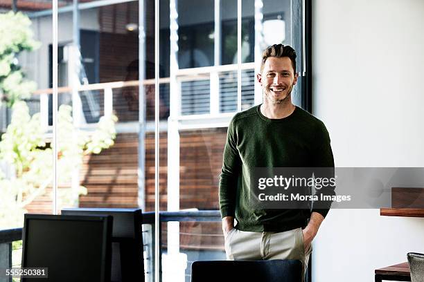 happy businessman standing by window in office - welvaart stockfoto's en -beelden