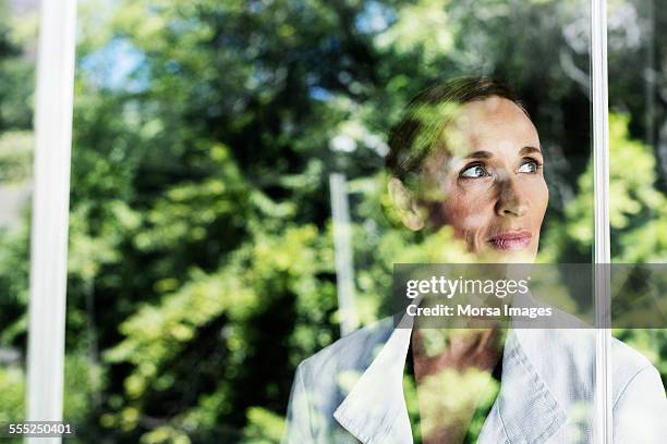 thoughtful businesswoman by glass window - glass reflection in office stock pictures, royalty-free photos & images