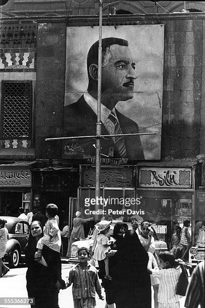 Under a large banner that depicts Egyptian President Gamal Abdel Nasser, pedestrians, some with children, walk on a city street, Cairo, Egypt, 1970.