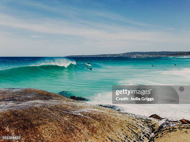 looking out off rocks at surfers on a summers day - bay of fires - fotografias e filmes do acervo