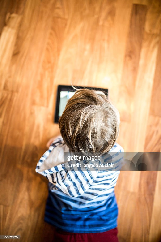 Young boy plays with mobile tablet on wood floor