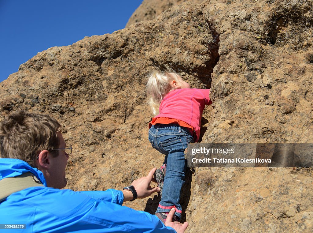 Father helping his baby daughter climb a rock