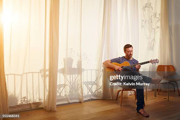 40's couple in apartment - man playing guitar photos et images de collection