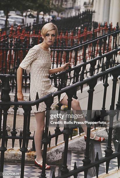 Sixties Fashion - English model Twiggy wears a textured cream coloured mini dress whilst standing on steps next to cast iron railings in Ladbroke...