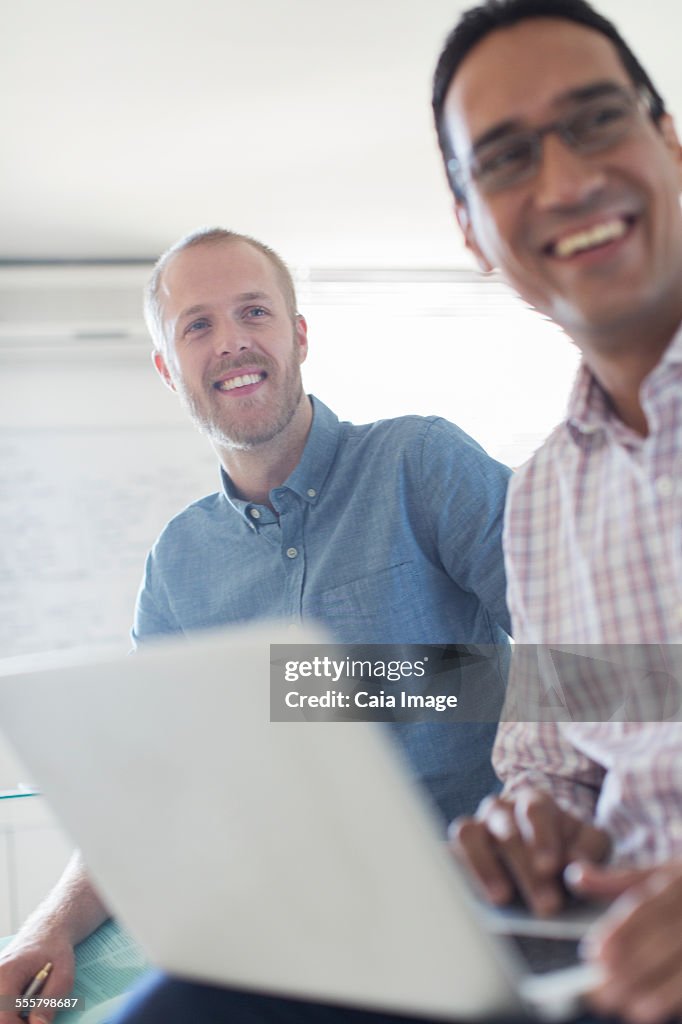 Two smiling businessmen using laptop in office