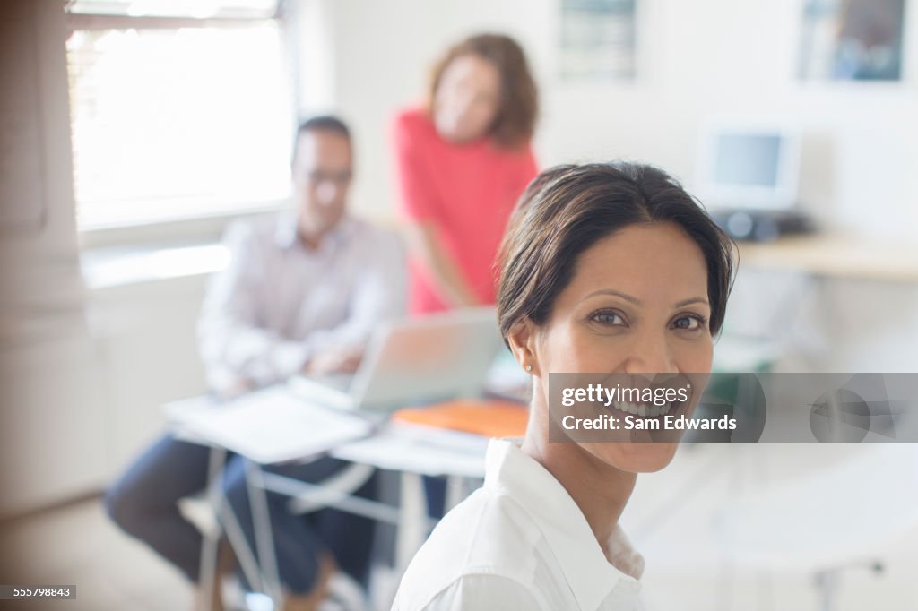 Portrait of smiling businesswoman in office, colleagues working in background