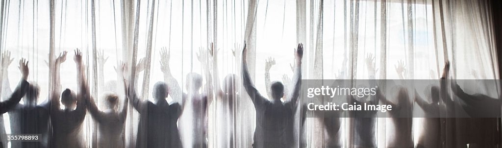 Silhouette of people raising hands behind transparent curtain