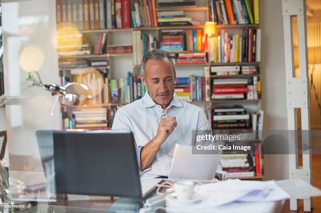 Businessman reading paperwork at home office desk