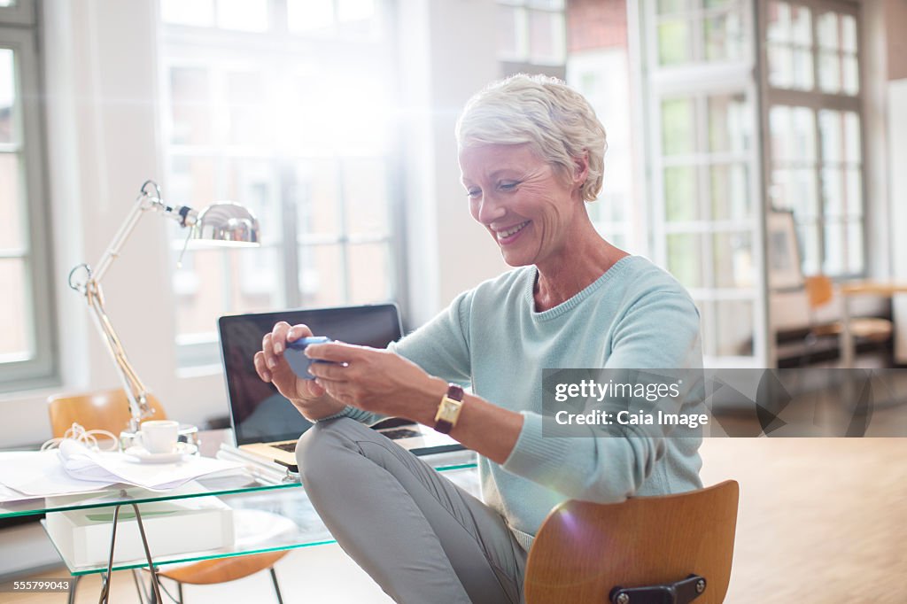 Businesswoman using cell phone at home office desk