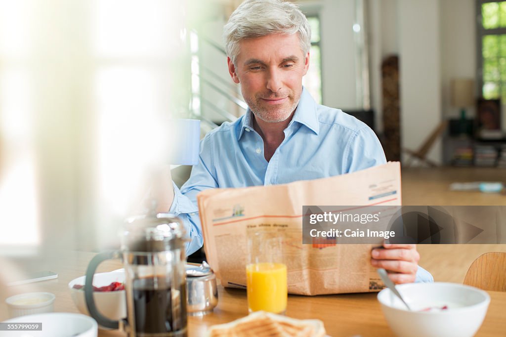 Older man reading newspaper at breakfast table