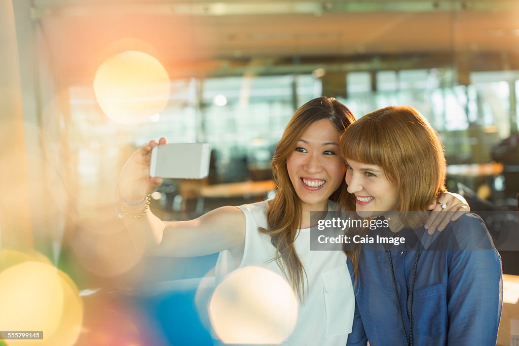 Businesswomen taking cell phone selfie in office