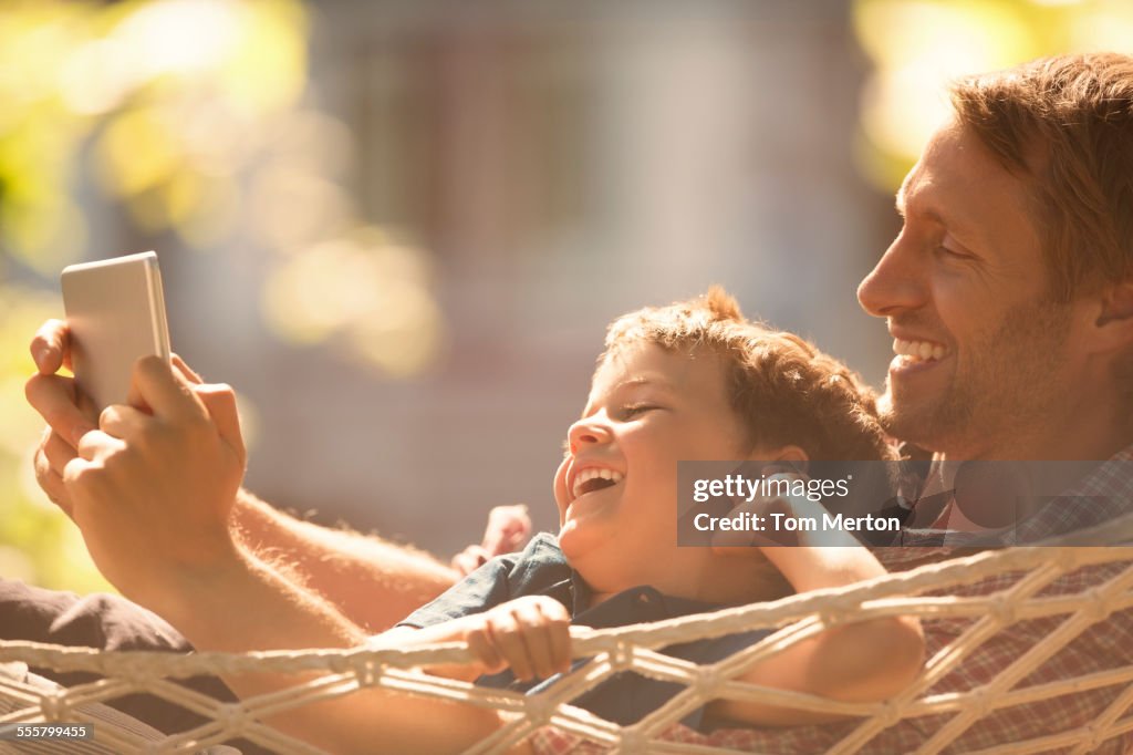 Father and son using digital tablet in hammock
