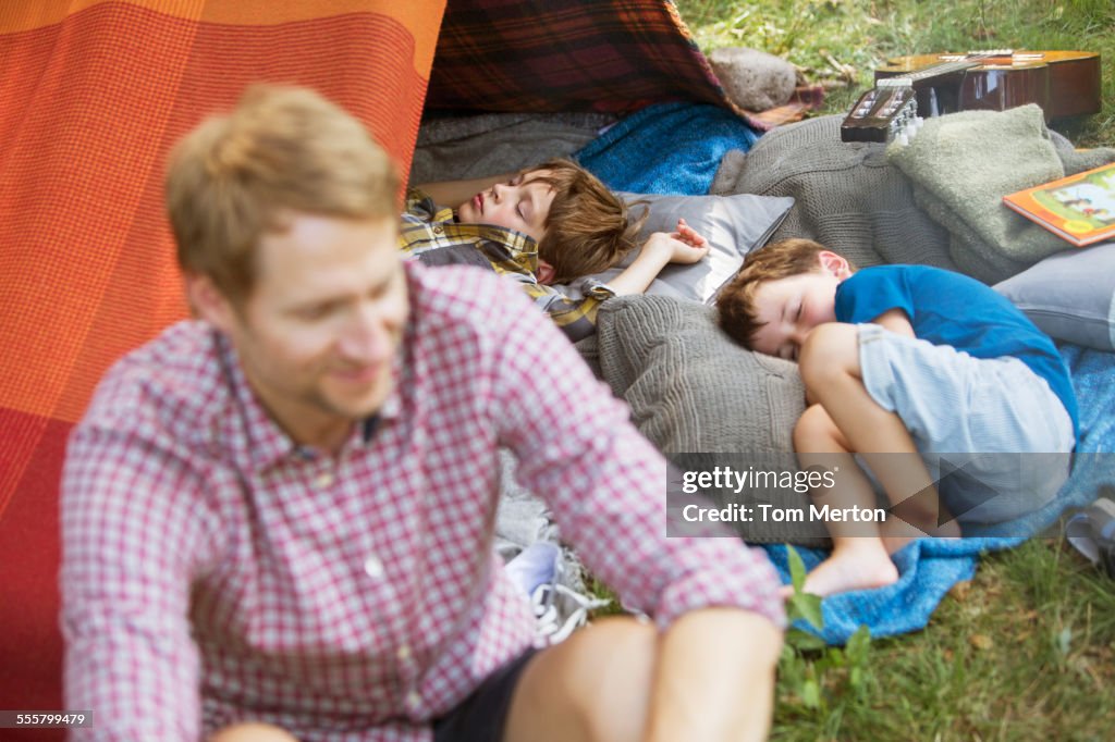 Padre sentado con hijos dormidos en la tienda de campaña